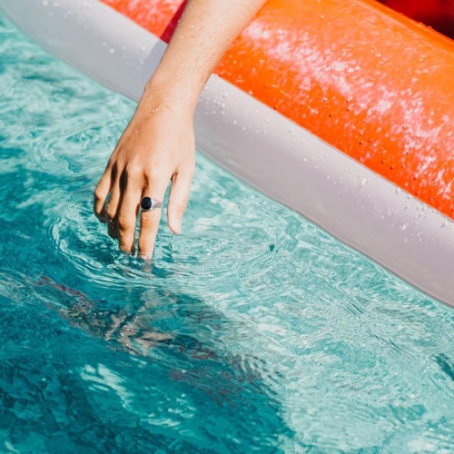 woman dangles her hand in the pool as she floats in an inflatable vessel